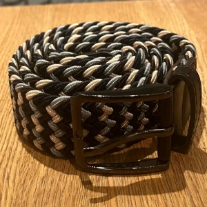 Flätat bälte  - Grisch bälte Färg svart/beige/grå Passar till allt och alla  Stretchigt tyg 