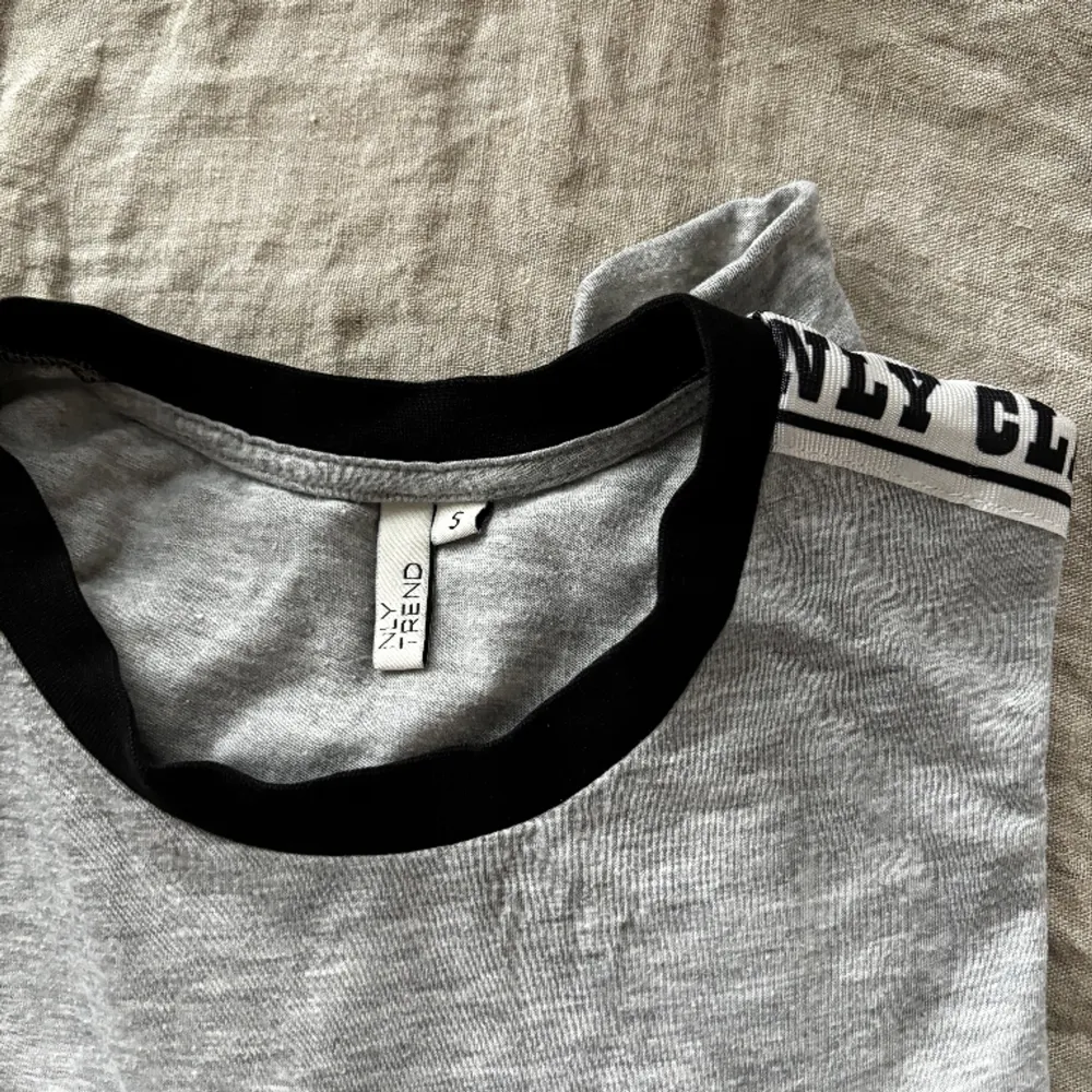 Grå crop top med en remsa med ”NLY CLASS OF 1999” längs med axlarna, som ger t-shirten en cool street-style.. T-shirts.