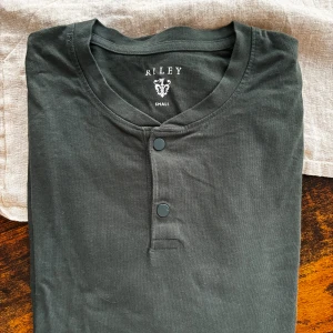 Mörkgrön Riley tröja - Mörkgrön långärmad tröja från märket Riley med två knappar vid kragen.