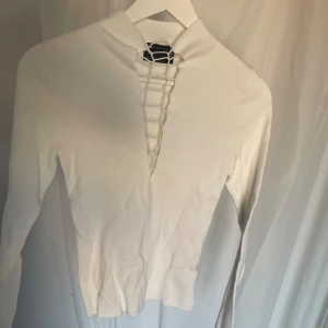 Vit tröja med snörning från Bershka - En vit långärmad tröja från Bershka med snörning framtill. Tröjan har en hög krage och är tillverkad i ett stretchigt material.