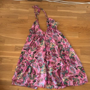 Sommarklänning  - Rosa sommarklänning med mönster. Den har öppen rygg och Knuts runt nacken och i ryggen. Köpt på marknad och alldrig använd