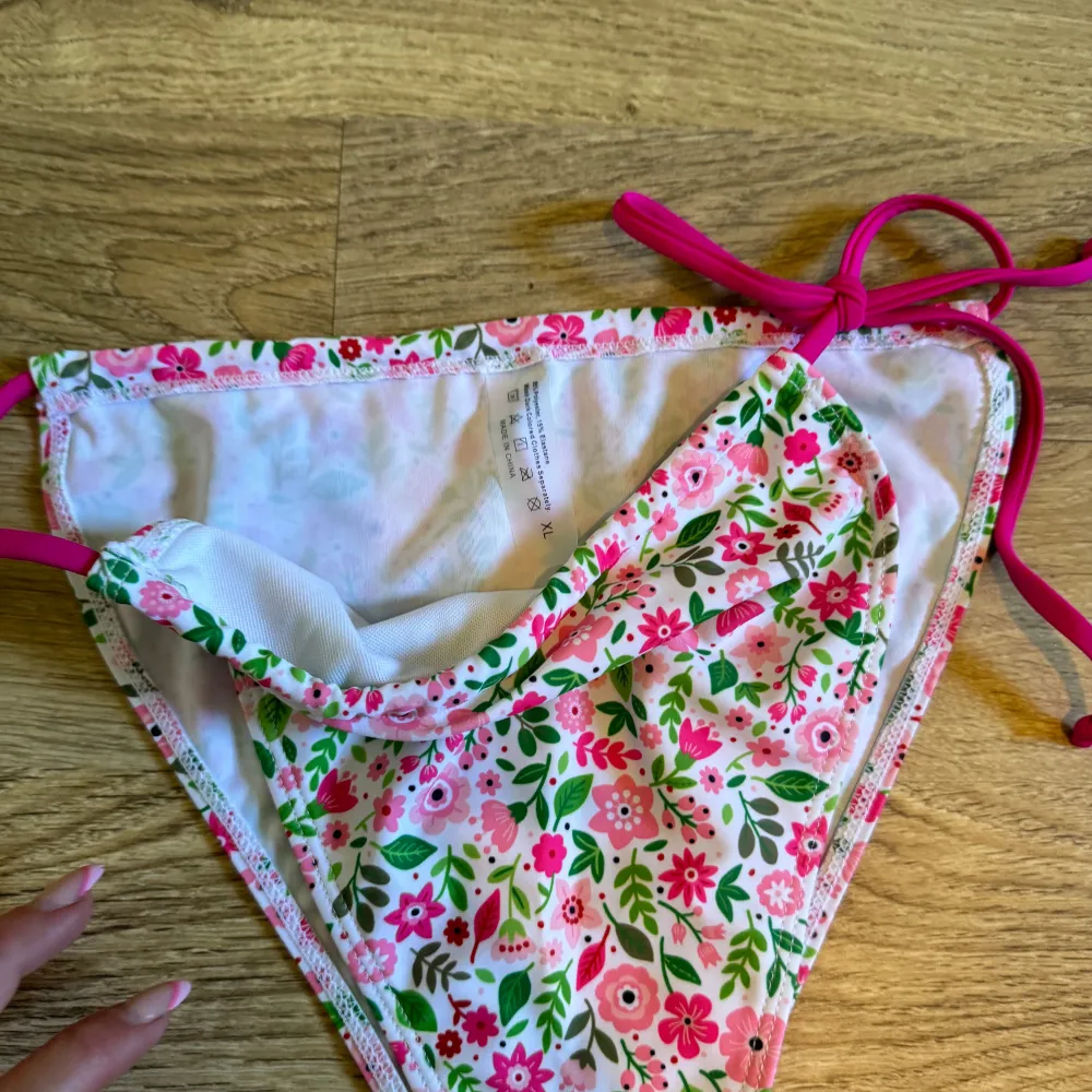 En färgglad bikiniunderdel med blommigt mönster i rosa, grönt och vitt. Underdelen har knytband på sidorna för justerbar passform. Helt ny.. Muu.