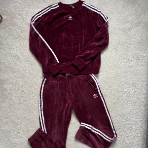 Adidas mjukisdress i Plysch stl S  - Fin Adidas dress med byxa och tröja i stl S! En fin vinröd färg!   Pris för både byxa och tröja  350:- + porto (postnord skicka lätt)   Kan mötas i Uppsala annars skickar jag kläderna! 