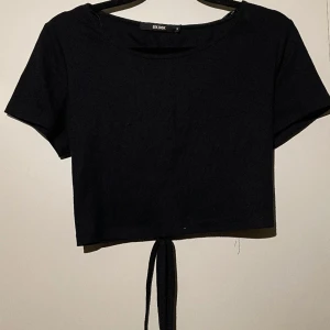 Svart kortärmad med knyte bak - Kort ärmad tröja som har snören, knyten bak till. Det är väldigt långa snören som du antingen kan göra en rosett med bak eller knyta runt magen- som man vill. Storlek M men sitter som en S enligt mig.  Ser grå ut på sista bilden men den är svart. 