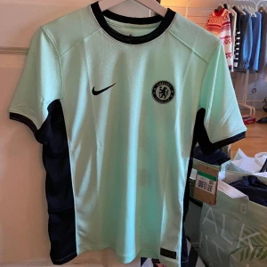 Chelsea tredjeställ 23/24 - Chelseas tredjeställ för säsongen 23/24 i färgen mingrön ✨ Helt ny och unisex! Storleken är XL barn och motsvarar XS/S för vuxen. Nypris - 1178 kr