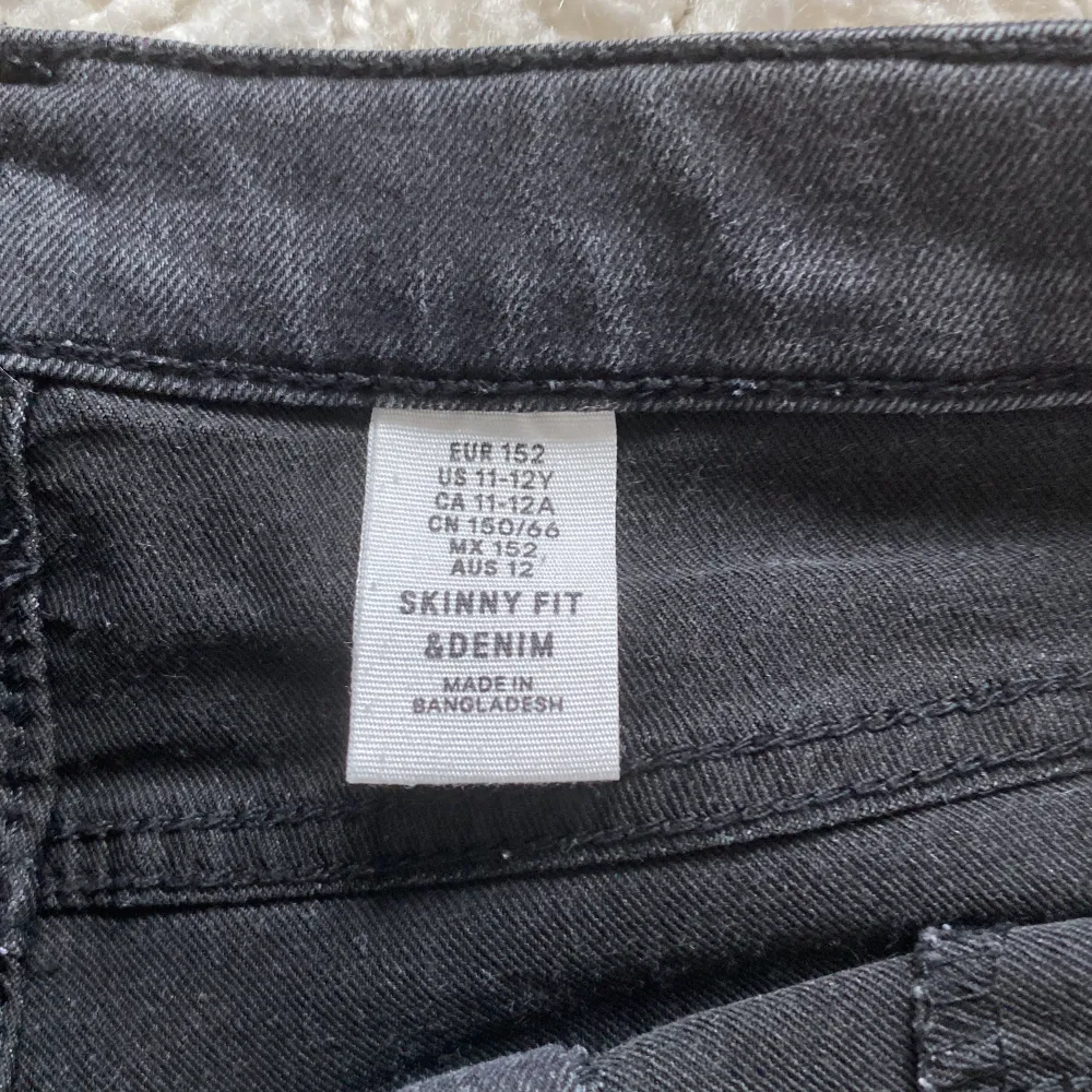 Ett par svarta skinny fit jeans i storlek 152. Byxorna har en knapp och dragkedja framtill samt fickor både fram och bak. Tillverkade i Bangladesh.. Jeans & Byxor.