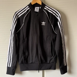 Svart träningsjacka från Adidas - Adidas SST tracksuit topp, byxor finns även men i storlek S - Använd 2-3 gånger - Priset ej hugget i sten - Kan mötas upp i Västerås 📍kvitto finns, skriv för fler bilder