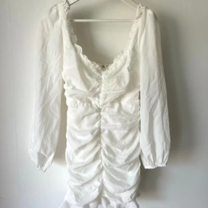 Vit klänning - Vit klänning med volang! Använd 1 gång (student). Har dock fått en fläck från en bläckpenna (se bild) men syns knappt på eftersom det är baksidan.