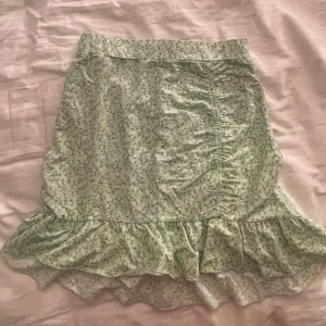 Grön blommig kjol från Gina Tricot - Säljer en superfin grön blommig kjol från Gina Tricot i storlek S. Kjolen har en volangdetalj längst ner och är perfekt för sommaren. Den är i nyskick och har en normal passform. Materialet känns som bomull och den är väldigt bekväm att ha på sig. Perfekt för både vardag och fest!
