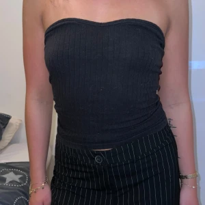 Svart ribbad tubtopp - Säljer en snygg svart ribbad tubtopp i storlek S. Perfekt för sommarens alla fester eller en utekväll med vännerna. Toppen är tight och sitter bra på plats. Den är ärmlös och axelbandslös vilket gör den superbekväm och luftig. Passar till både jeans och kjol!