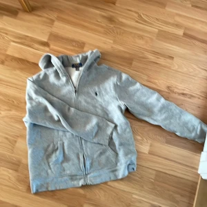 Grå hoodie från Polo Ralph Lauren - Säljer en grå hoodie från Polo Ralph Lauren i storlek s .Den har en dragkedja framtill och två fickor. Insidan är fodrad med mjuk fleece vilket gör den extra varm och mysig. Perfekt för kalla dagar!