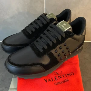 Svarta sneakers från Valentino Garavani - Ett par svarta sneakers från Valentino Garavani med svarta nitar på sidan och svarta snören. Skorna har en robust sula och en elegant design.
