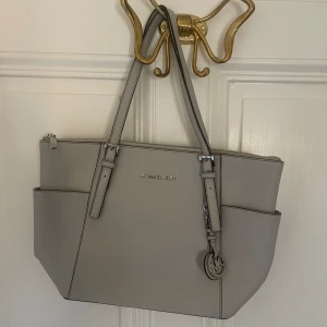 Michael Kors Väska - Äkta superfin Michael Kors Väska ljusgrå i bra skick. Köpt i NK, nypris 2795kr. Pris kan diskuteras. 💌