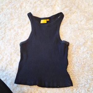 Svart ribbad linnetopp från Gina Tricot - Säljer en snygg svart ribbad linnetopp från Gina Tricot. Toppen är ärmlös och har en tight passform.  Materialet är mjukt och stretchigt. storlek 146/152 men passar xs-xxs