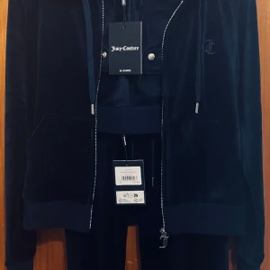 Juicy Couture-set NYSKICK - Oanvänt set med hoodie och byxor i stl. S. Prislapp kvar.   Färg: Mörkblå,  (BLUE DEPTHS) Material: Velour  Stl: S