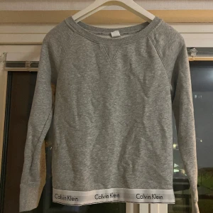 Calvin Klein tröja - Grå Calvin Klein tröja med deras logga som resorband längst ner på tröjan. Använd några fåtal gånger så fortfarande i väldigt bra och fint skick. Köparen står för frakten. Betalning sker via swish.