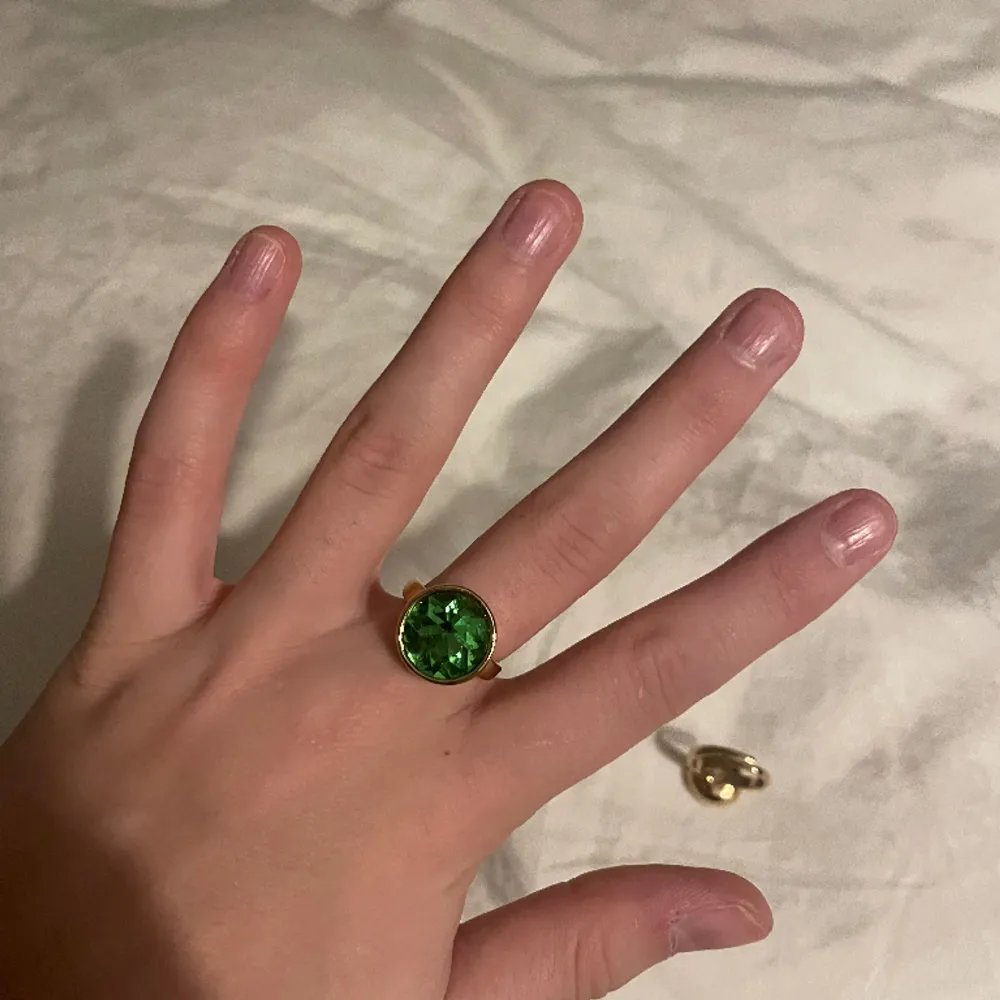 Guldpläterad ring med grön kristall. En symbol för hopp till din smyckessamling. Justerbar storlek med kristall på 15 mm i diameter. 100 % glam piece. Tillverkad av minst 75 % återvunnet material. Nypris är 400kr och den är helt oanvänd!!!. Accessoarer.