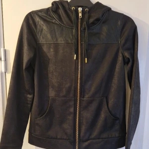 Huvtröja med skinndetaljer - Väldigt snygg huvtröja i glansigt tyg och skinndetaljer längst upp.