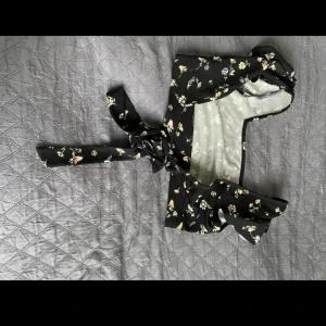 Svart blommig knytblus från Shein - En svart blommig knytblus från Shein. Blusen har ett blommönster i vitt och gult och är designad med långa knytband som kan knytas runt midjan och öppen i ryggen 💕