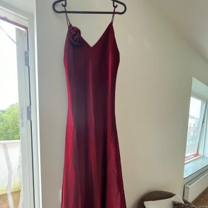 Röd balklänning  - Jätte vacker balklänning med fin rosdetalj. Den är ganska lång och har ett tillhörande extra tyg som är till för att ha över armarna. Använd 1 gång! 