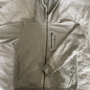 Sailracing  - En grå ziphoodie från Sailracing i storlek S. En liten defekt (fläck) på högerärmen (bild 2) som inte syns vid användning men värd att nämna. Nypris ≈ 1500kr.  Priset kan självklart diskuteras!