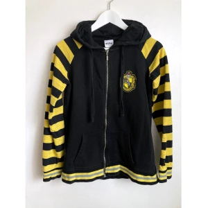 Hufflepuff huvtröja, S/134, barn, Harry Potter, hoodie, sweatshirt, munkjacka - Hufflepuff huvtröja, broderi på bröstet, tryck på ryggen, raglanärm. Aningen urtvättad. Mått i cm: bröstvidd 46; längd mitt bak 61; ärmlängd mätt från halsen 67. 