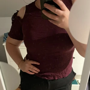 Vinröd Blus/t-shirt - Söt vinröd blus med snygga detaljer vid axlarna, både öppna vid axlarna samt knutna snören vid början av ärmen. Strl S/M 45kr  Köparen står för frakten💕