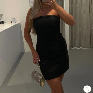 Glittrig kort klänning - Jättefin svart glittrig klänning från astrid frank nyårskollektion. Säljer denna oanvända klänning pga att jag beställde två men glömde skicka tillbaka den som var förliten. Nypris är 570kr + frakten på 99kr. Köparen står för frakt.