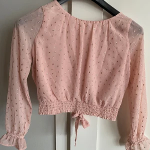 Söt blus i puderrosa strlk 146 - Sötaste blusen i svagt rosa med glittriga detaljer. Resår nedtill och snygg detalj med knytning bak. Tunna genomskinliga ärmar. Riktigt fin och väldigt fint skick. Snygg till både vardag & fest. Från H&M, strlk 146.  Rök- & djurfritt hem. 