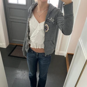 Grå kofta från Abercrombie & Fitch - Grå zip hoodie från abercrombie & fitch i storlek M. Fint skick förutom att dragkedjan är lite guppig vilket syns på bild 1 & 2. Använd gärna köp nu!