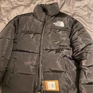 The north face jacka (Nytt) - Denna helt nya och oanvända jacka från The North Face är både funktionell och stilren. Den är tillverkad av högkvalitativa material och erbjuder vattenavvisande egenskaper för att hålla dig torr. Den har en modern design. Second class