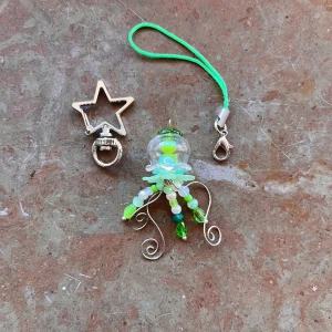 Grön manet 💚🪼 - En liten manet där du kan välja att ha som en nyckelring eller en phonecharm!⋅˚₊‧ ଳ⋆.ೃ࿔*:･  Med en nyckelring kostar det 5kr extra!   Maneten har glas komponenter så var försiktig! <3  Skriv i DM först, tack! ༊彡