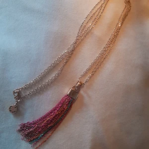 Långt Halsband - Ett långt halsband med guldfärgad kedja och färgglad metall"tofs", från bud&rose. 45 cm långt (när det är knäppt). Köpt på Åhléns och i mycket gott skick. 