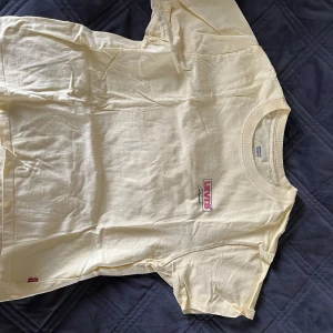 Ljusgul Levi’s T-shirt  - En ljusgul T-shirt som passar bra till vår och sommar. Fin rosa detalj. Lite kortare i modellen men sitter väldigt fint, säljer då jag växt ur den.
