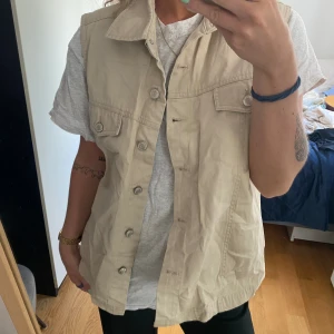 Armlös jeansjacka  - En armlösjenasjacka/väst i beige, står ingen storlek eller märke men skulle säga M/L