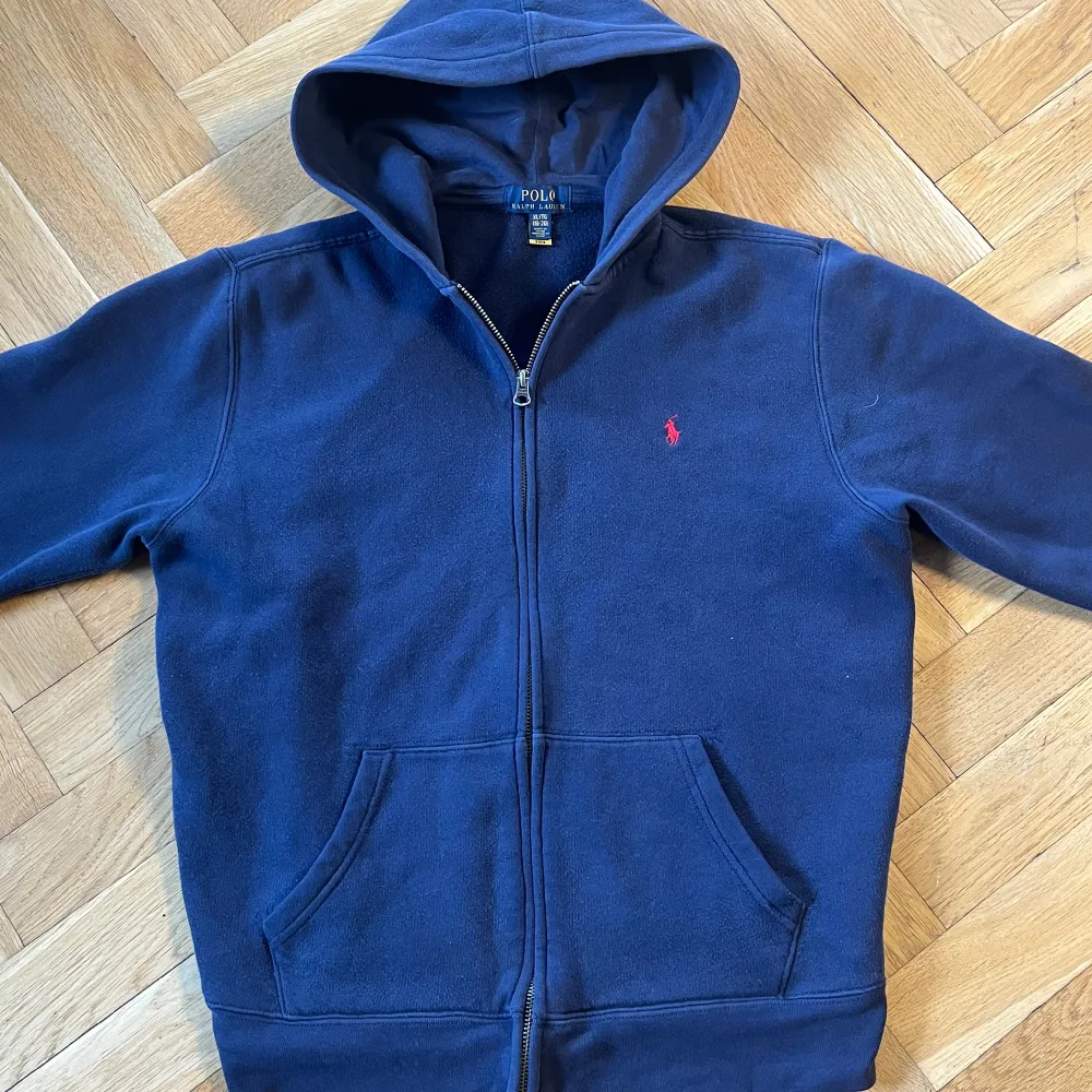 Säljer denna marinblåa Ralph lauren hoodie som är i storlek 170 vilket motsvarar small. Har sytt inne i den för att få bättre passform och de är inget som syns utifrån. Den är i 9/10 skick och inga defekter. Priset kan diskuteras. Hoodies.