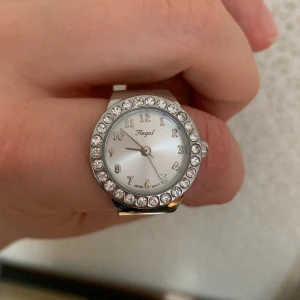 Klockring - En ring med en klocka på i fräscht skick! Batteriet är tyvärr urladdat men det går att byta ☺️Bandet är uttöjbart och är vanligtvis  en aningen större storlek.