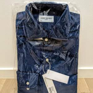 Ny, blå John Henric-skjorta i denim med originaletiketter och -emballage. Storlek 40.  Nypris: 1000 kr  Hämtas på Ön i Malmö eller skickas per post.