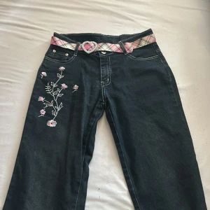 Jeans med blomdetaljer  - Jätteeeesöta lågmidjade jeans med rosa blomdetlajer på!! Köpta här på Plick, men passar tyvärr inte längre😿 Skärpet ingår och går att ta av också!!