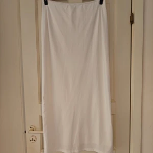 Vit långkjol  - Vit långkjol Aldrig använd, köpte nyligen men kom ej till användning Kjolen har en slit på baksidan, når ner till marken för mig som är 173 cm lång. Den har 2 lager så är inte direkt genomskinlig, beror ju självklart på vad man har under.  Stretchigt