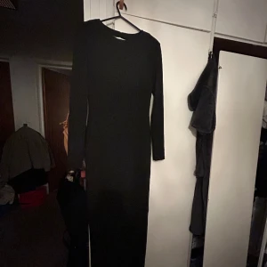 Svart långklänning med öppen rygg och slits bak  - Jätte fin klänning, använd en gång då jag ej har tillfälle för denna något mer! Jätte skönt material! Går ner till golvet på mig med klackar (är 160cm). Har även kuddar på axlarna så den får en fin form på!  Ny pris 650kr