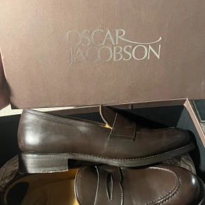 Oscar Jacobson Penny Loafers Slip-ins Mörk lerbrun Strl 42 - Kan mötas upp centralt i Sthlm eller skickas mot frakt.  Säljes då de tyvärr är för små samtidigt som datum för öppet köp passerat. Endast använda en(1) ynka gång så passa på! Skokartong och skopåsar ingår. Materialet i skinn, KAP!  Nypris: 2799 :-