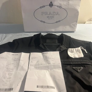 PRADA – Pikétröja – KVITTO + MYCKET BRA skick! - PRADA!  Använd högst 4-5 gånger. Inköpt i Stockholm på Birger Jarlsgatan. Inkluderar exklusiv Prada-kasse, extraknapp, förvaring för knapp och självklart kvittona som tillsammans med etiketter intygar äkthet.  Inköpt för 9300 SEK. MYCKET BRA skick!