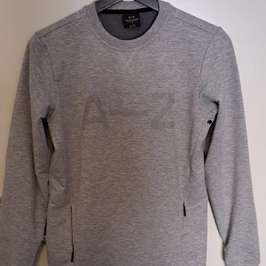 Grå A-Z sweatshirt - Grå långärmad tröja med 2 framfickor med dragkedja  Saknas storlek men skulle säga att den passar en S, ytterst lite stretch dock