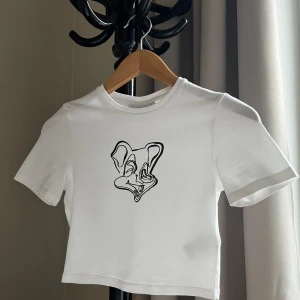 Croptop med tryck - Fin vit croptop från Weekday med grafiskt tryck i storlek XS. Material 95% bomull 5% elastan. Endast använd ett fåtal gånger, inga defekter, som ny!  Kan fraktas eller mötas upp i Göteborg.