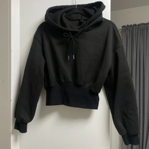 Svart hoodie - Svart kort hoodie med luva, stretchig vid midjan. Köpt för 200kr säljer för endast 59kr. Storlek XS men skulle passa som S också.