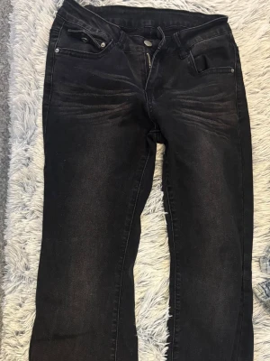 Svarta utsvängda jeans - Snygga svarta utsvängda jeans med lätt slitning och klassisk femficksdesign. Jeansen har dragkedjegylf och silverfärgade nitar. Perfekta för en trendig och avslappnad look.