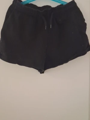 Svarta shorts med snörning - Svarta shorts med elastisk midja och snörning framtill. De har en enkel och avslappnad design, perfekta för varma dagar. Tillverkade i mjukt material som känns skönt mot huden.