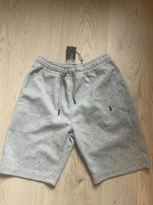 Grå shorts från Polo Ralph Lauren - Snygga grå shorts från Polo Ralph Lauren med elastisk midja och snörning. Klassisk passform med två sidofickor perfekta och fina shorts! OBS lappen är inte kvar men finns kvar om man vill ha den.