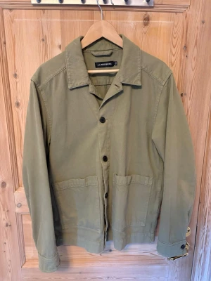 Olivgrön overshirt från J.Lindeberg - Stilren olivgrön overshirt från J.Lindeberg i 100% bomullstyg. Klassisk krage, knäppning framtill med svarta knappar och två stora fickor framtill. Perfekt lager på lager-plagg med avslappnad passform och snygga detaljer.